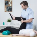 Male physiotherapist exercising with patient having knee pain